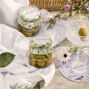 Aceitunas Verdes Bella di Cerignola Fratepietro en escena de aperitivo con mantel blanco, flores y copa