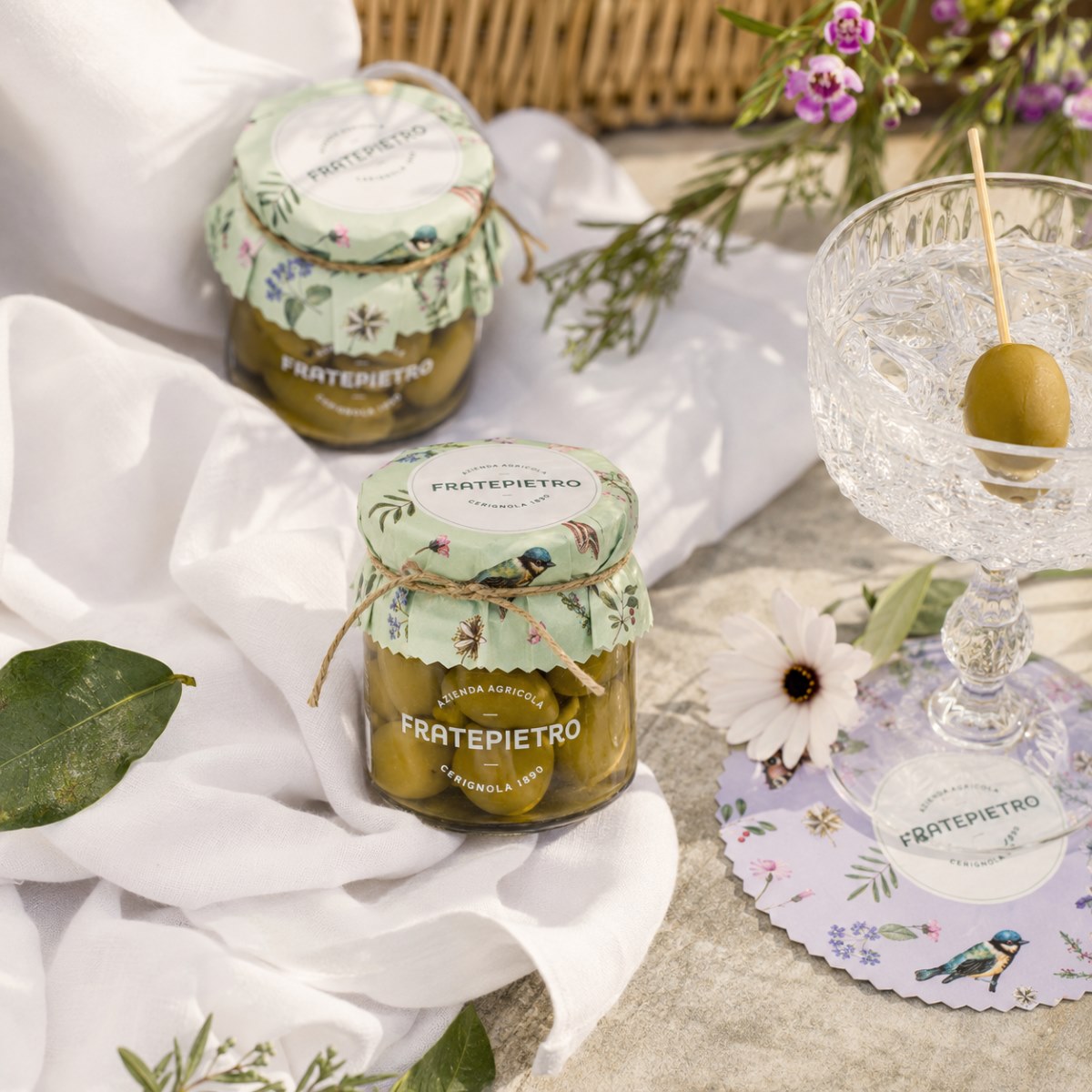 Aceitunas Verdes Bella di Cerignola Fratepietro Aperitivo Aceitunas Verdes Bella di Cerignola Fratepietro en escena de aperitivo con mantel blanco, flores y copa