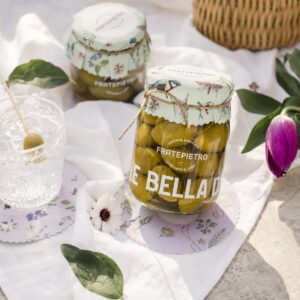 Aceitunas Verdes Bella di Cerignola Fratepietro en escena decorativa con mantel blanco, flores y vaso de aperitivo