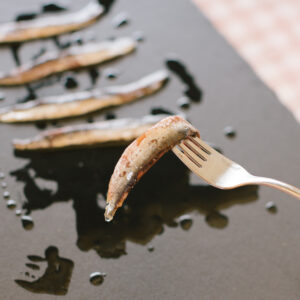 Anchoa de Santoña Reserva con piel servida en un tenedor, sobre plato de pizarra con aceite de oliva.