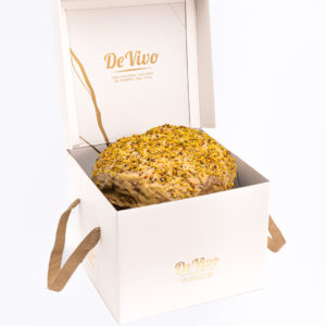 Panettone al pistacho de Pasticceria De Vivo en caja premium blanca abierta, con glaseado y granillo de pistacho, fotografía profesional para tienda gourmet.