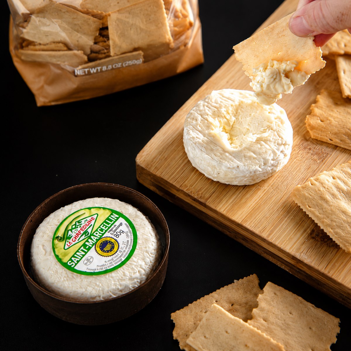 Queso Saint-Marcellin IGP Le Chartreuxin 80 g con crackers Queso Saint-Marcellin IGP Le Chartreuxin 80 g servido con crackers en tabla de madera
